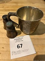 Group view of handled cup and two shakers on wood surface with auction card.