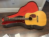 Acoustic guitar laid in open black hard shell case with red interior