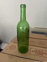 Single green glass wine bottle photographed on a cardboard box surface, showing the shape and color of the bottle clearly.