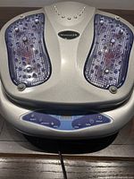 Top view of the silver and blue electric foot massager showing textured footpads and control buttons.