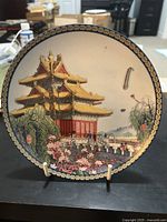 Front view of the porcelain plate featuring a traditional Chinese pagoda and people flying kites in a spring setting with cherry blossoms and greenery, with a decorative gold and black border.