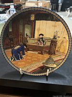 Front view of decorative plate depicting a historical scene with traditional Chinese figures and detailed interiors, bordered with ornate gold pattern.