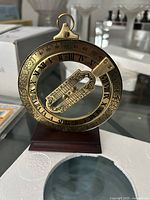 Close-up image of the brass Franklin Mint ring dial sundial showing roman numerals and ornate engravings, mounted on a wooden base.