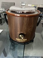 Front view of a brown woodgrain Crock-Pot slow cooker with clear glass lid and black handles showing the control knob and brand name.