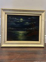 Frontal photo of the framed velvet oil painting showing a nighttime scene with a full moon, clouds, and trees near water.