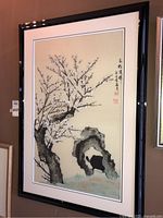Framed Asian-style ink wash painting showing a plum blossom tree, bird, and rock formation in a black glossy frame.