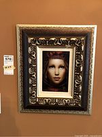 Full view of the framed art piece on the wall showing the ornate frame and artwork.