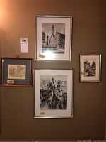 Four framed black and white art prints mounted on a wall. Various building and urban street scenes including a castle and street labeled prints.