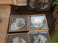 Four framed ceramic plates featuring Asian themed artwork with figures in traditional attire, each mounted in wooden frames and blue mats.