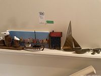 Shelf display of all items showing metal sailboat, wooden house, fishing boat with lobster, wooden seagulls, and coastal village print