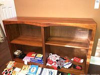 Front view of solid wood bookshelf showing two shelves and wooden finish, with some contents on floor in front.