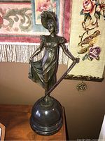 Front angle showing full statue and base, statue holding dress and cane with detailed hat.