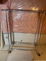 Full view of the adjustable height metal clothing rack with two horizontal bars and four wheels.