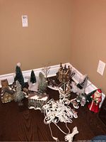 Overview of four ceramic village buildings, bottle brush trees, figures and string lights