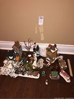 Group shot of all buildings, figurines, ornaments, sleigh, logs and lights on hardwood floor.
