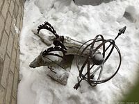 Two-piece metal garden art set on snow-covered ground, includes spherical metal sculpture and bird on driftwood base