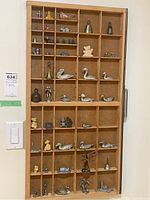 Full view of wooden display shelf with numerous miniature figurines including metal birds, animals, human figures, and toys arranged in compartments