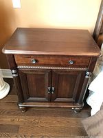 Front view of one wooden side table with drawer and two-door cabinet with round knobs, showing turned legs and casters.