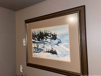 Framed winter coastal watercolour painting hanging on wall showing full view