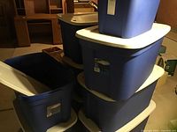 Stacked large blue plastic storage totes with white lids, showing 7 totes stacked and 2 separate with lids off or on
