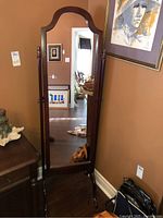 Full view of the wood framed swivel mirror standing on the floor against a wall, showing its arched top and dark wood finish with decorative finials.