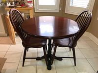 Full view of round wooden table with 2 spindle back chairs in a kitchen/dining area