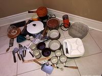 Overview of all vintage cookware, servingware, cutlery and coffee grinder items arranged on floor.