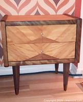 Front view of nightstand showing two-drawer design, veneer pattern and brass-capped legs