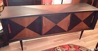 Front view of mid-century modern walnut sideboard with three sliding doors featuring triangular contrasting panels