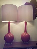 Front view of two burnt orange table lamps with white drum shades placed side by side on a wooden table.