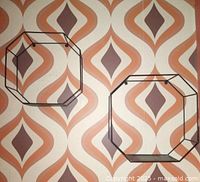 Two black metal octagonal wall shelves mounted against a retro patterned wallpaper, showing size difference and shape.