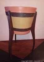 Front view of plant stand showing orange, yellow painted planter with black metal band and three dark wooden legs.