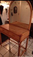 Front angle view of the vintage bamboo and rattan vanity table with the arched mirror and two drawers visible.