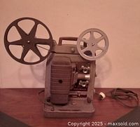 Side view of vintage Bell & Howell 8mm projector showing film reels, lens assembly, and handle.