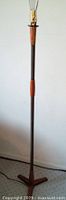Full view of the floor lamp, showing teak wood accents on wood base, coiled metal shaft, and lamp socket with pull chain