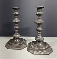 Pair of antique spelter metal candlesticks on neutral background showcasing front and side views