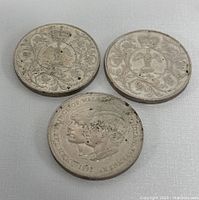 Photo showing obverse side of three coins displaying intricate floral and crown designs plus dual profiles on one coin.