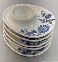 Stacked view of five white ceramic egg cups showing blue floral decoration on each.