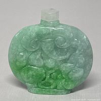 Front view of the oval jade perfume or snuff bottle showing detailed carved motifs and the green and white color variations.
