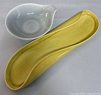 Yellow elongated celery dish and gray rounded ceramic bowl with pouring spout together on white background
