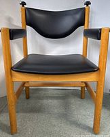 Front view of the armchair showing wooden frame, black leather seat, backrest, and armrests.