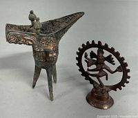 Photo showing a Chinese bronze wine cup with three legs and a pointed spout alongside a metal Nataraja statue depicting Shiva dancing within a circular halo.