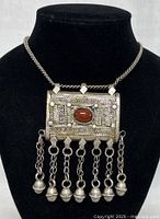 Front view of old Tibetan silver pendant necklace with red stone and chain tassels on black bust