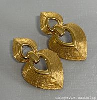 Front view of the pair of signed Christian Dior gold-tone earrings showing their heart-shaped textured design.