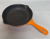 Top angle view of the frying pan showing the black cast iron cooking surface and orange handle and exterior with pour spouts.