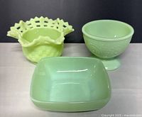 Photo showing three vintage custard glass pieces including a yellow basketweave ruffled candy bowl, a light green ornate pedestal bowl, and a smooth square bowl.
