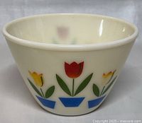 Front view showing red and yellow tulips in blue pots on cream-colored glass bowl.