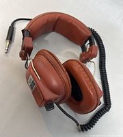 Full view of brown vintage Futura headphone resting on side showing padding, coiled cable, and 3.5mm plug