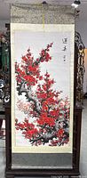 Full view of the silk scroll showing red plum blossom branches on a white silk background with fabric border in light and dark tones.