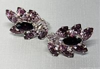 Two earrings laid side by side showing purple and clear rhinestones in cluster floral design